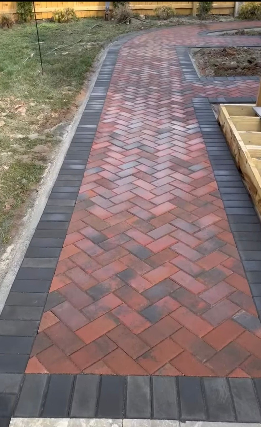 Red brick walkway with a dark border curving through a garden